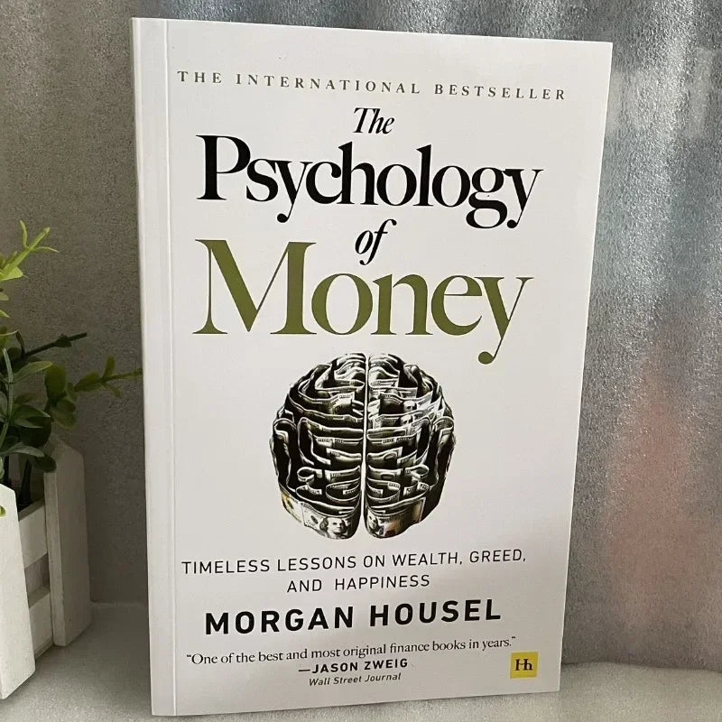 Book titled 'The Psychology of Money' by Morgan Housel on a gray surface with a plant in the background.