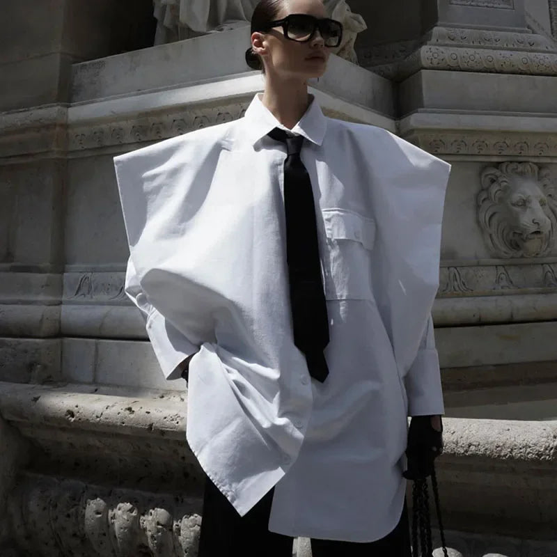 Person wearing a large white shirt with a black tie in front of a stone architectural background