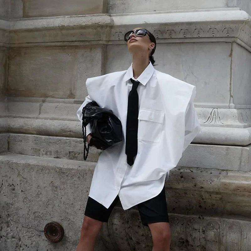 Person wearing a white shirt with a black tie and black shorts, standing on stone steps.