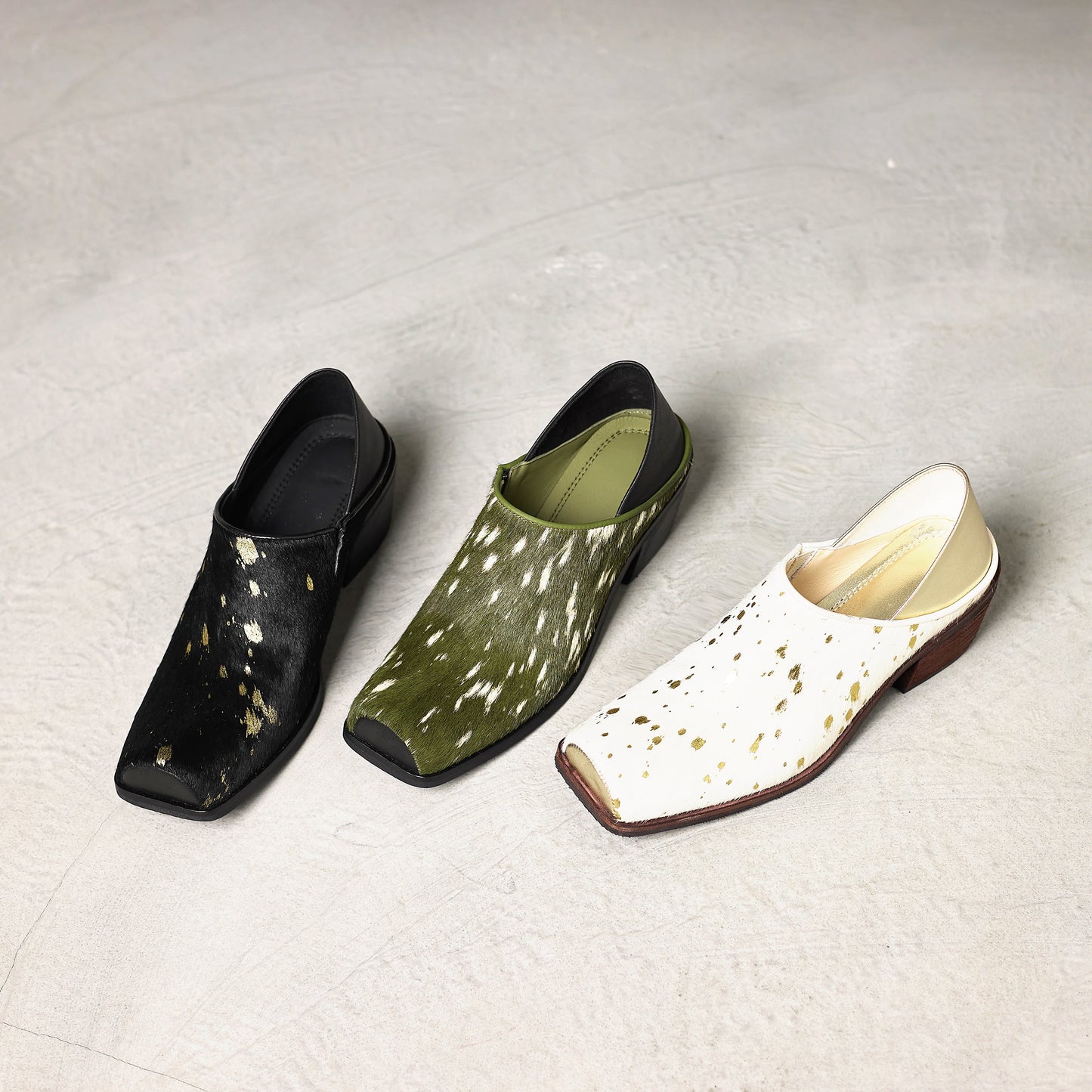 Three pairs of shoes in black, green, and white with gold speckles on a light gray background