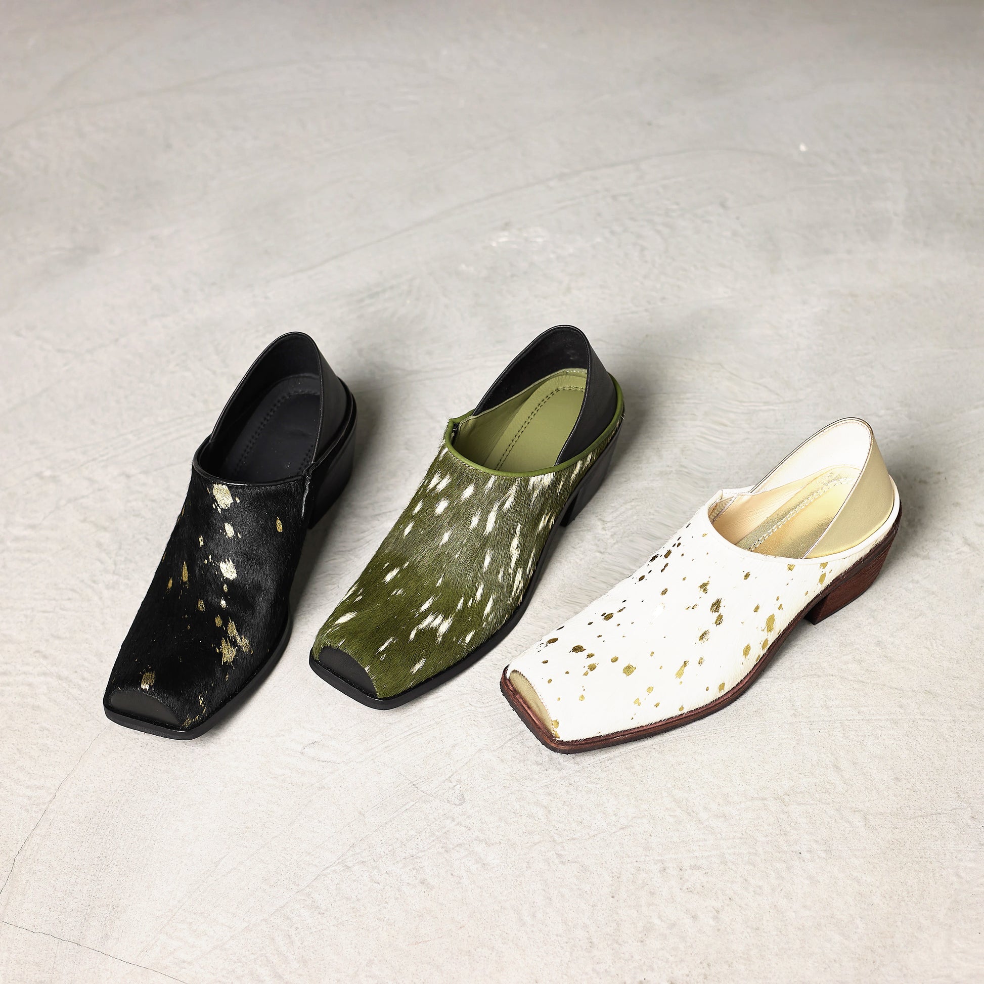 Three pairs of shoes in black, green, and white with gold speckles on a light gray background