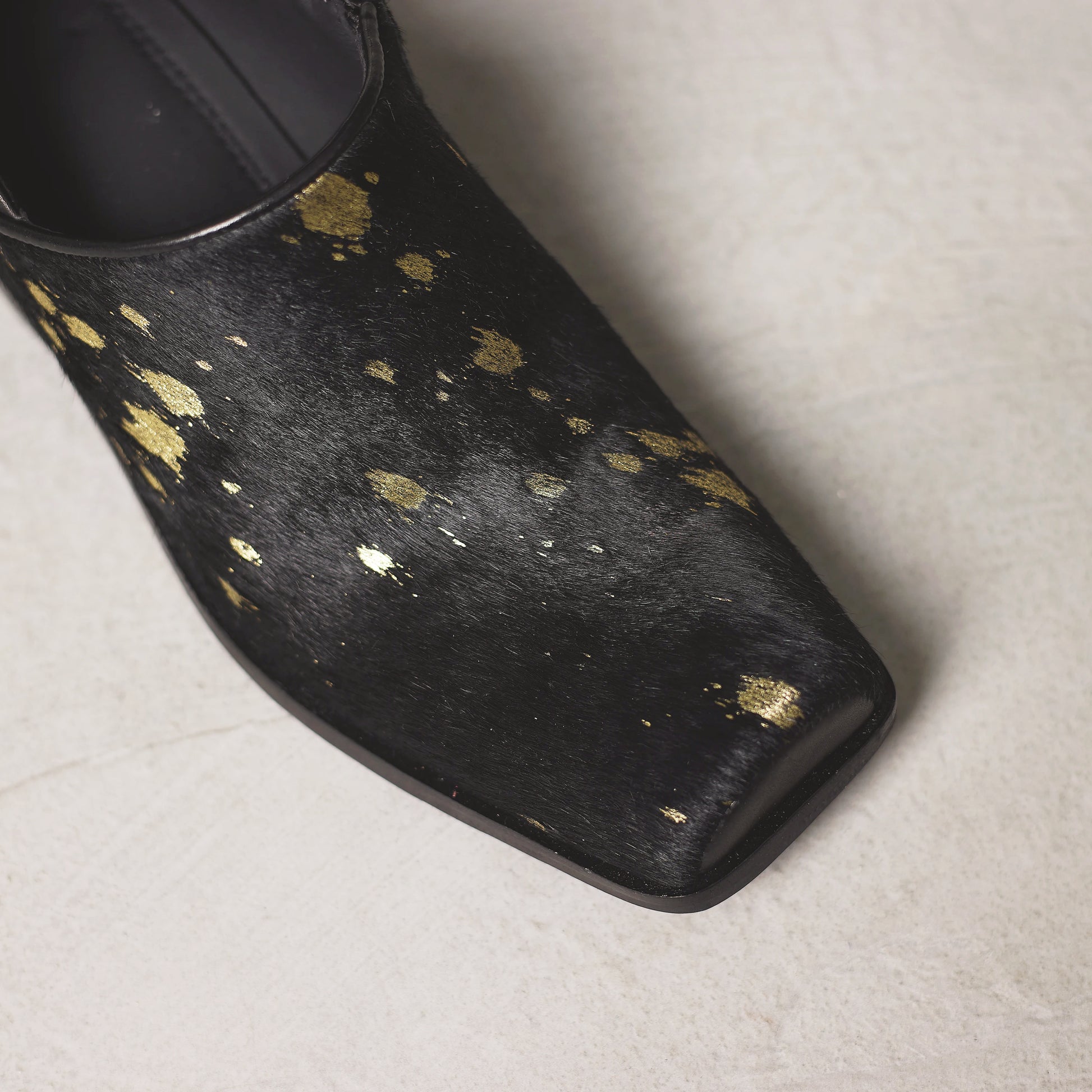 Black shoe with gold speckles on a light gray background