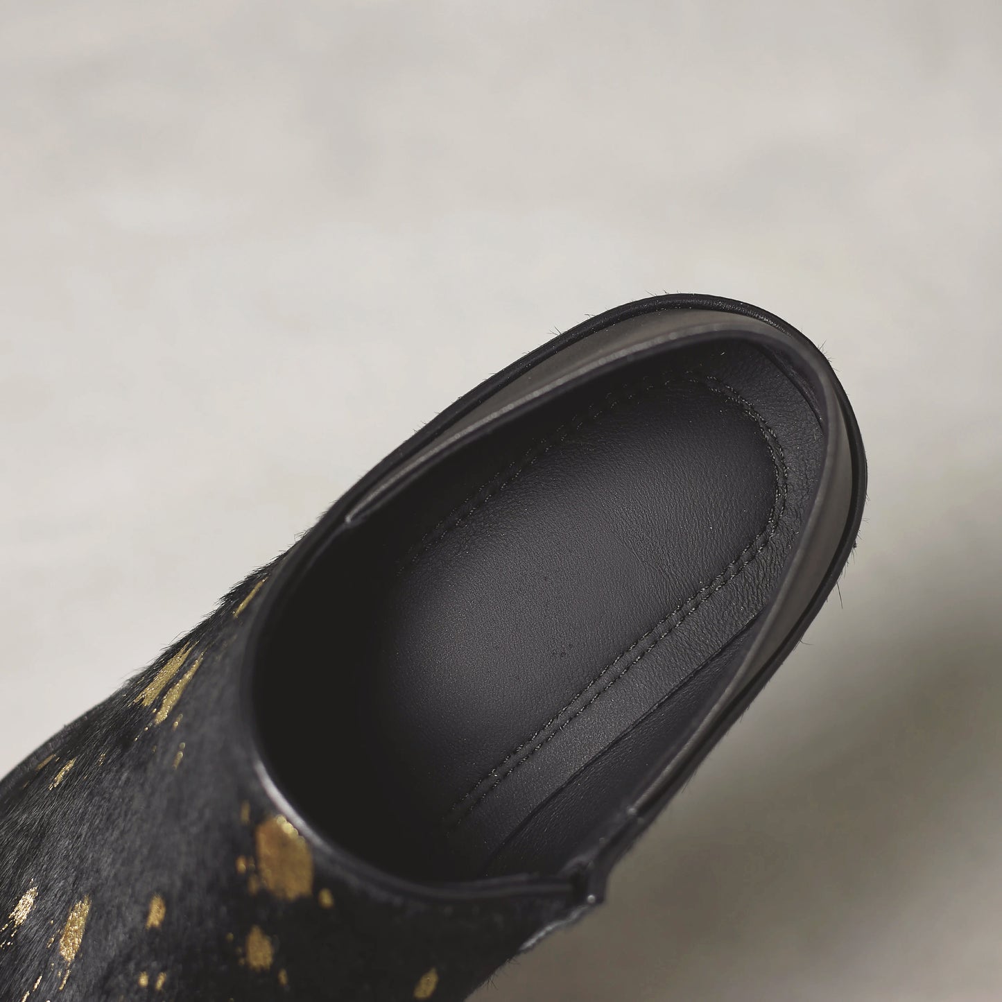 Black shoe with gold speckles on a light gray background