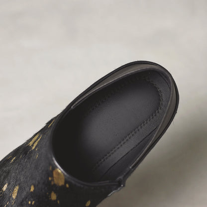 Black shoe with gold speckles on a light gray background