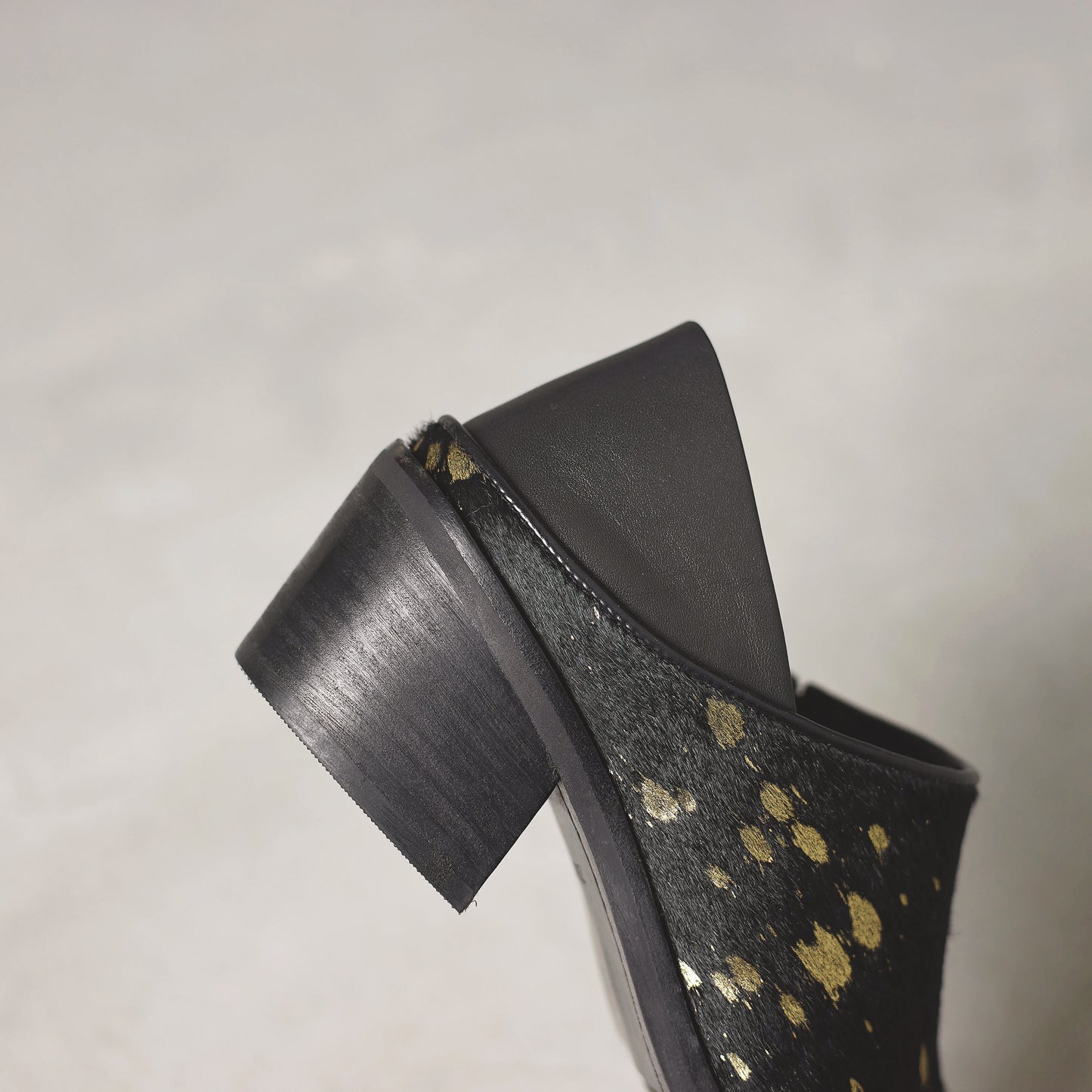 Black high-heeled shoe with gold polka dot pattern on a gray background