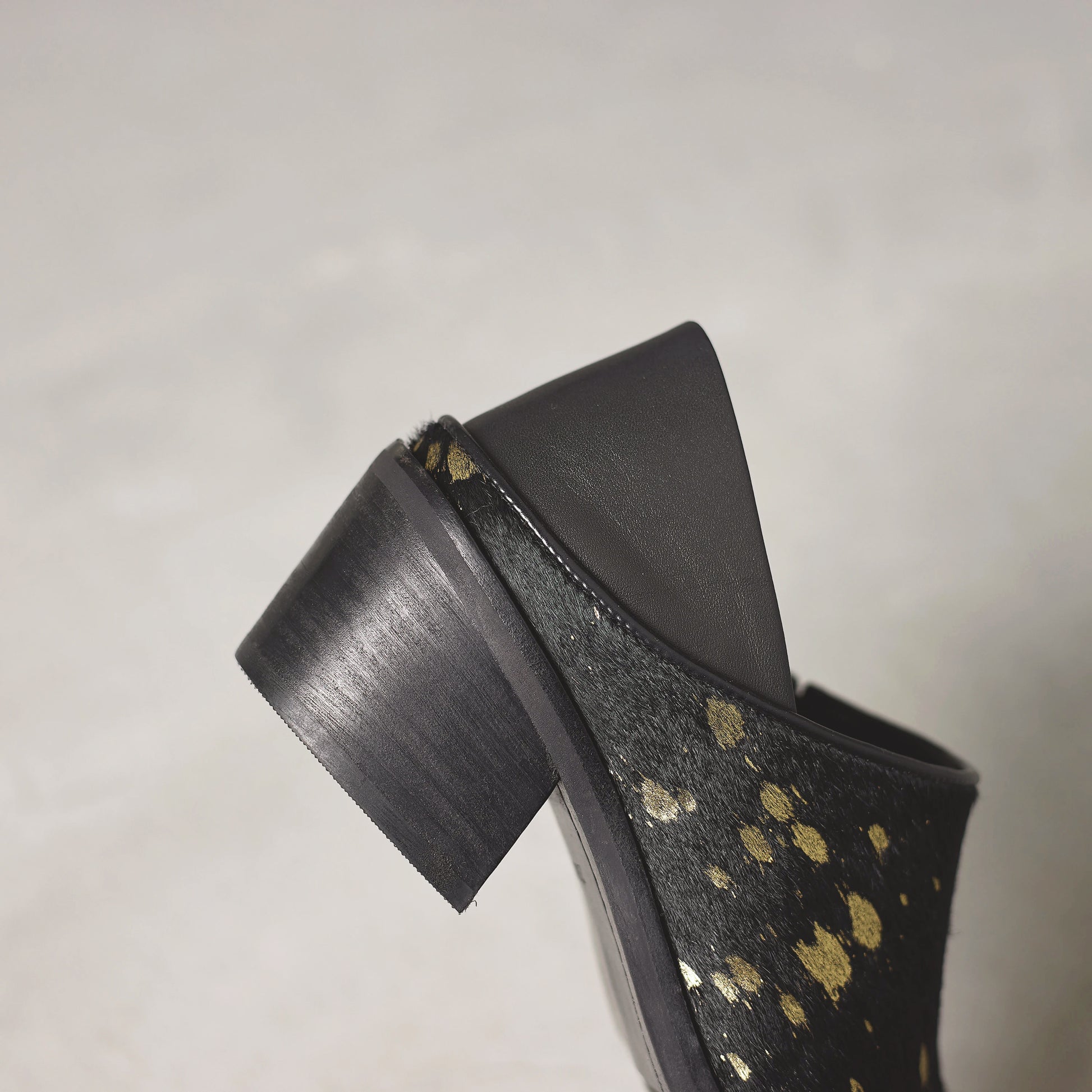 Black high-heeled shoe with gold polka dot pattern on a gray background