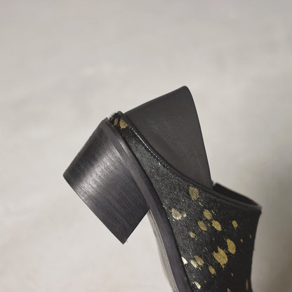 Black high-heeled shoe with gold polka dot pattern on a gray background