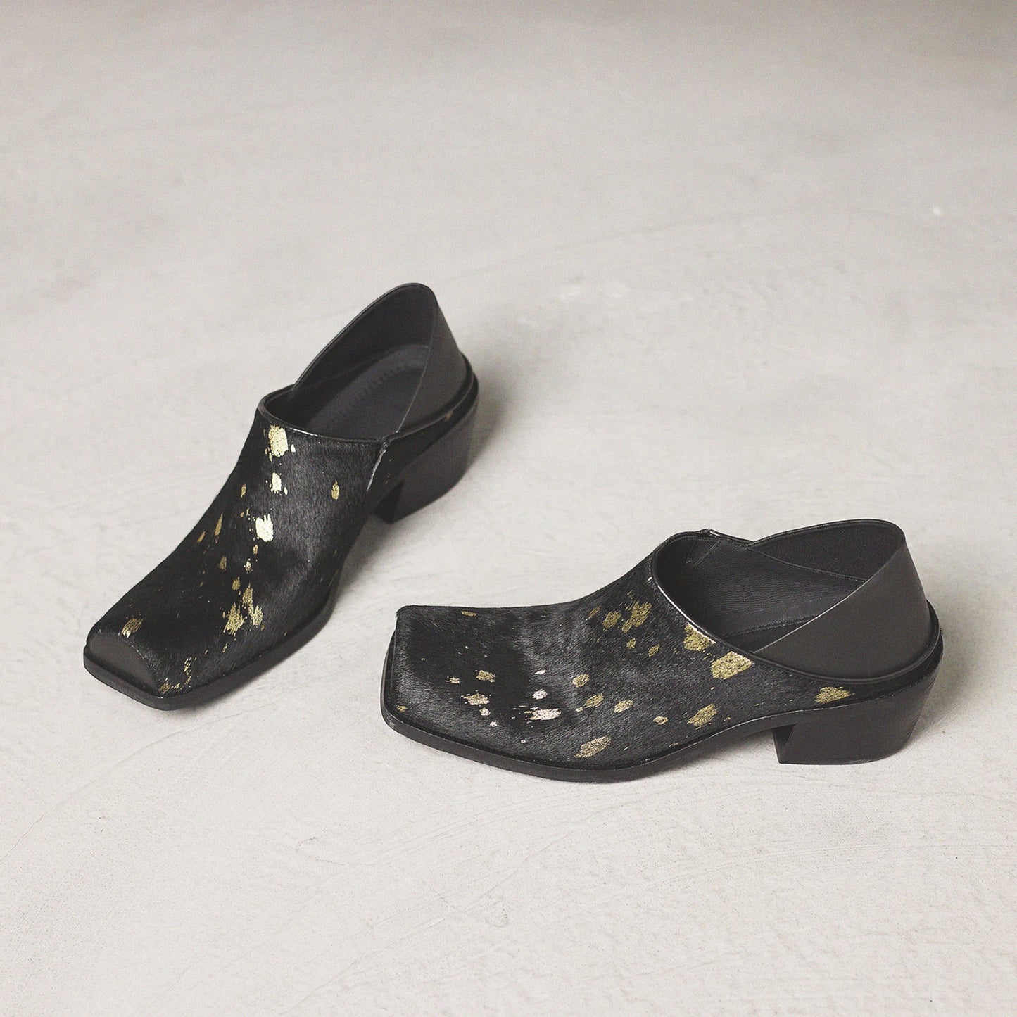 Pair of black clogs with gold speckles on a light gray background