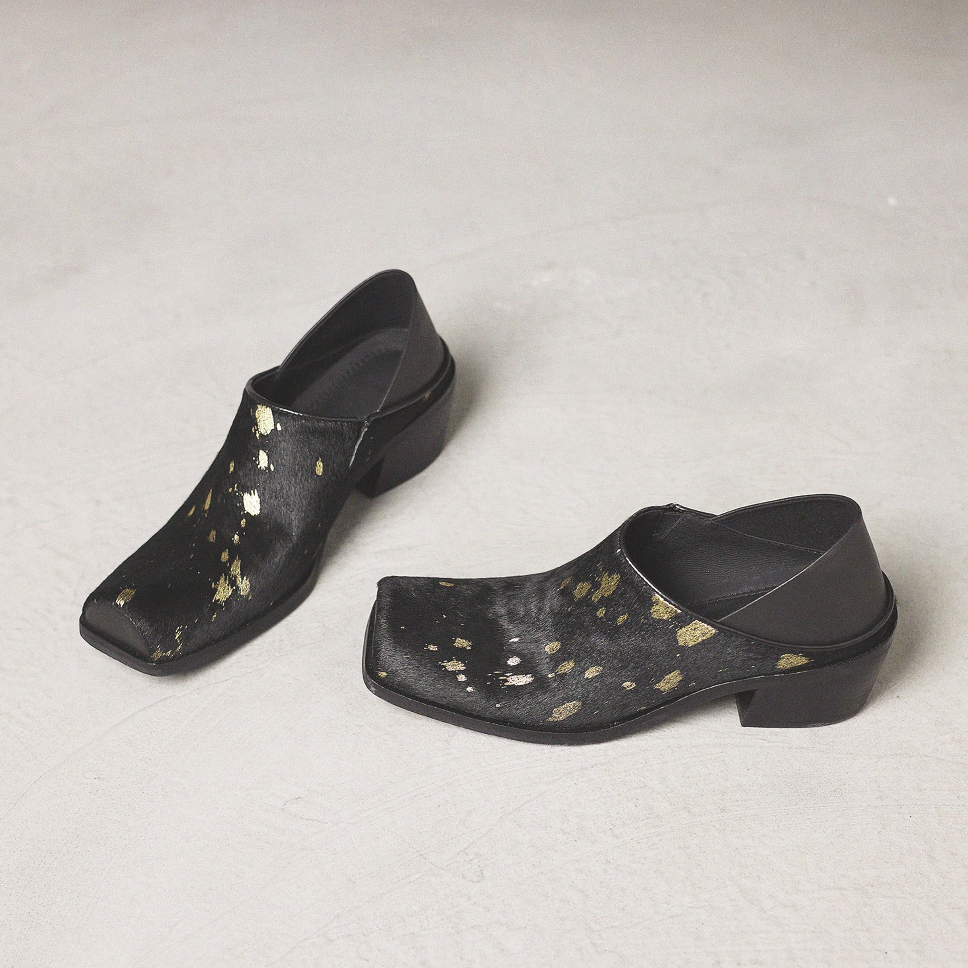 Pair of black clogs with gold speckles on a light gray background
