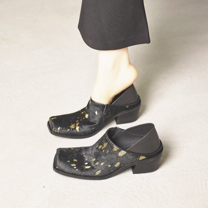 Black clogs with gold speckles worn by a person on a neutral background
