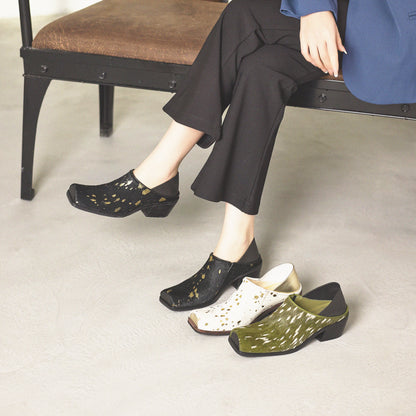 Person wearing black, white, and green shoes with a patterned sole on a light gray floor.
