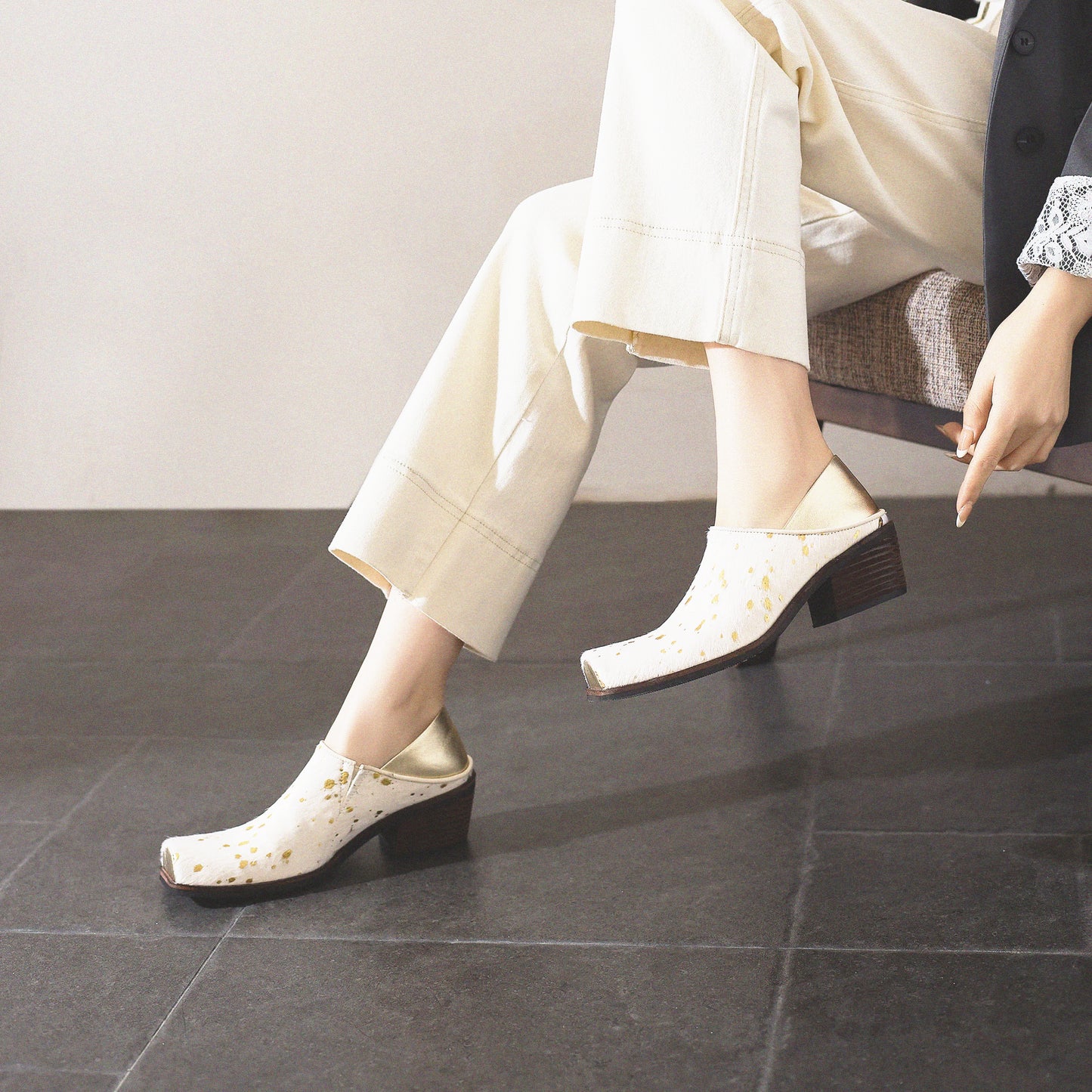 Person wearing white polka dot shoes sitting on a chair with a neutral background
