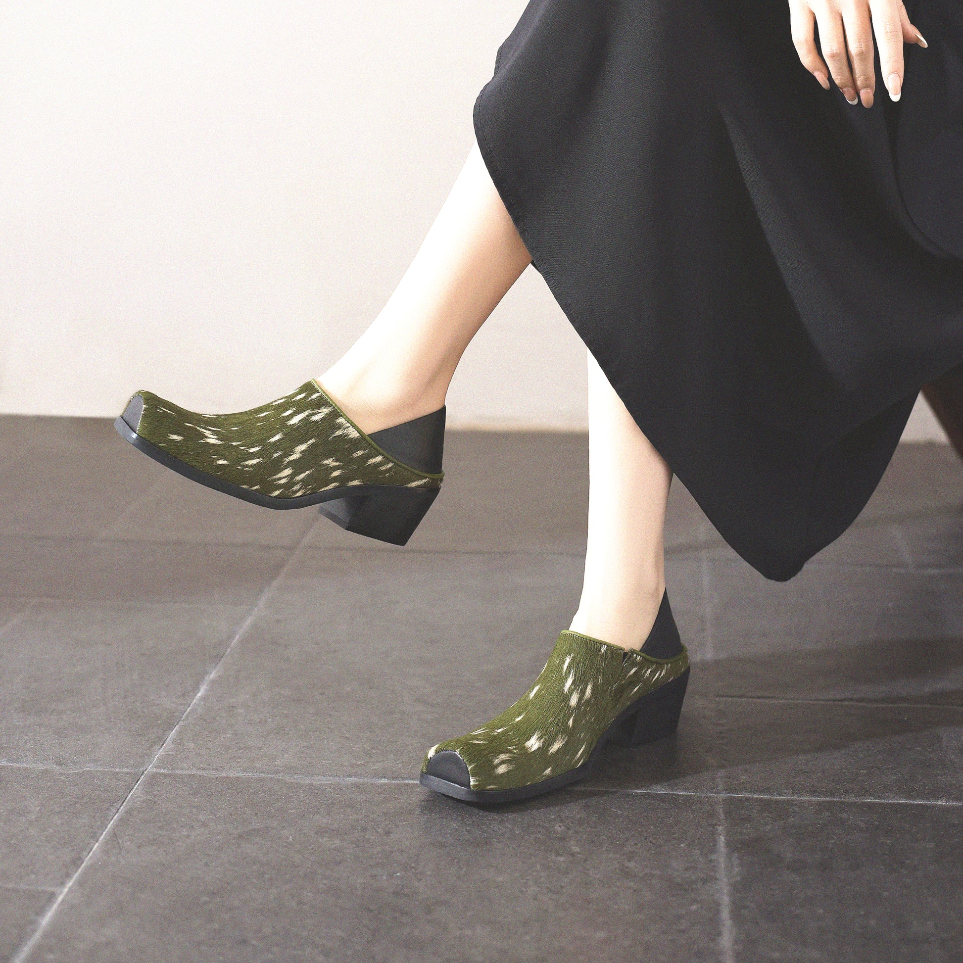 Green patterned shoes worn by a person sitting on a tiled floor.