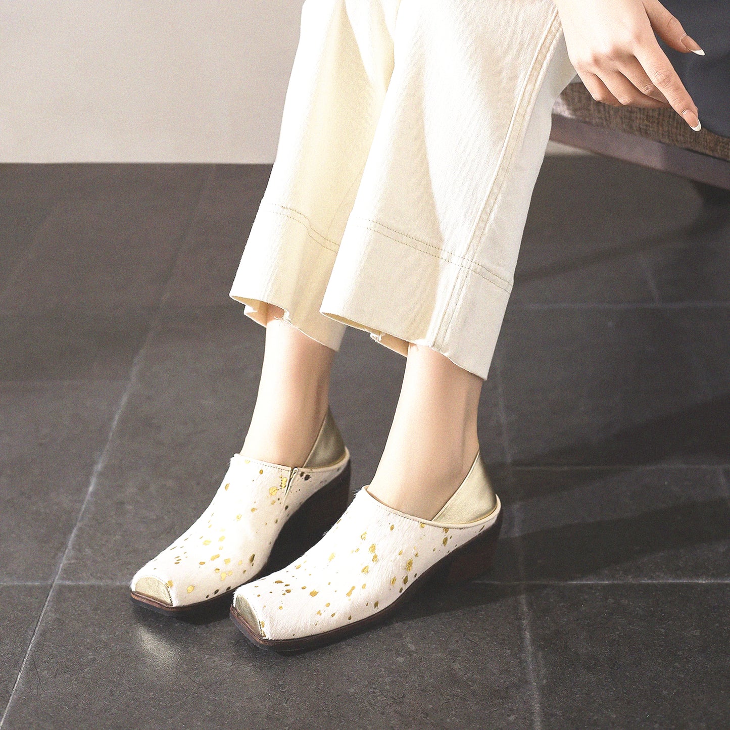White shoes with gold accents worn by a person sitting on a dark floor.