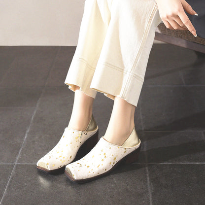 White shoes with gold accents worn by a person sitting on a dark floor.