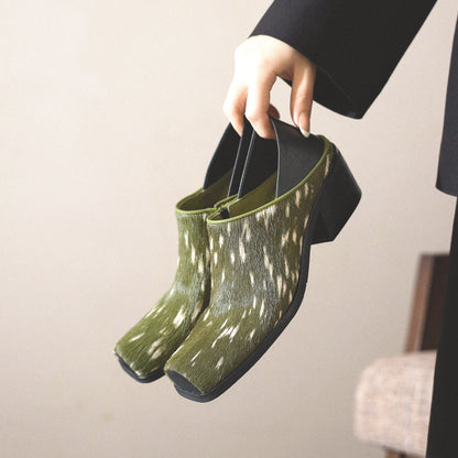 Green patterned shoes held by a person against a neutral background