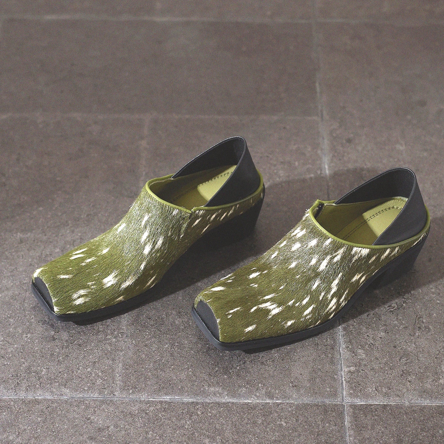 Pair of green clogs with black soles on a tiled floor