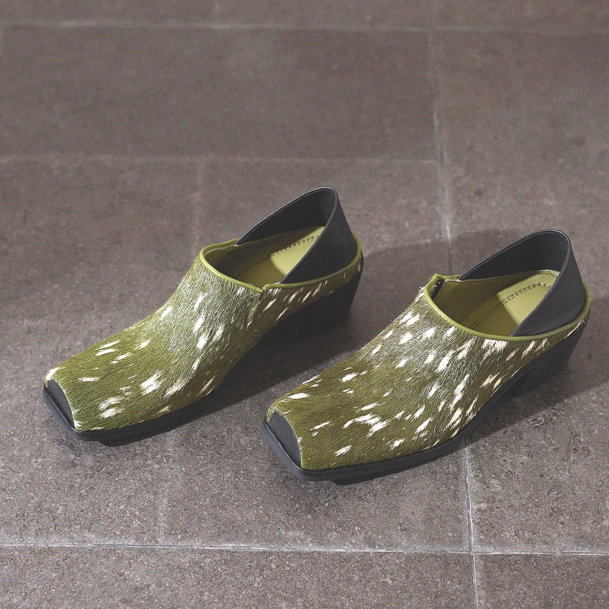 Pair of green clogs with black soles on a tiled floor